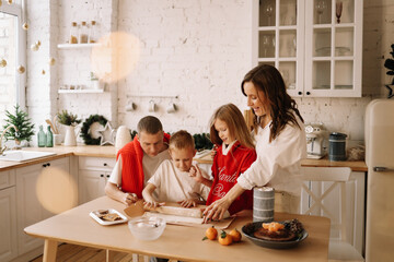 The concept of Christmas. A family with two children in sweaters prepare a festive food in the decorated kitchen in the house on a holiday. Two parents with their daughter and son have fun at home