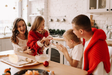 The concept of Christmas. A family with two children in sweaters prepare festive food have fun and play with flour in the decorated kitchen in the house on a holiday in winter in December at home
