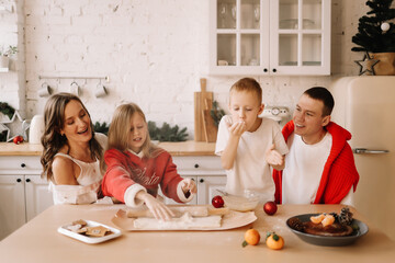 The concept of Christmas. A family with two children in sweaters prepare a festive food in the decorated kitchen in the house on a holiday. Two parents with their daughter and son have fun at home