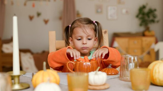 Happy Halloween! Little cute girl eating in the kitchen. Toddler girl in a pumpkin costume eating sandwiches on breakfast. Morning at home.