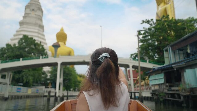 Young Asian woman tourist sitting on boat using smartphone taking photo of the giant buddha statue at the Wat Paknam Phasi Charoen temple in Bangkok, Thailand. Travel and transport lifestyle