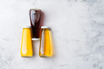 Bottles with yellow and red liquid halthy beverage on gray background. Orange apple cherry juice