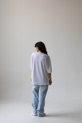 Fototapeta na wymiar Beautiful brunette with curly hair in a white t-shirt and oversized jeans. Mock-up. Back view.