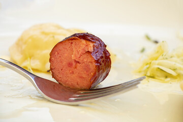 A piece of broken sausage and a fork lie on a white plate for lunch, a simple lunch