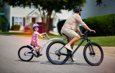 Fototapeta premium father and daughter, young kid cycling together. bicycle with towable bike trailer. active lifestyle for family with kids