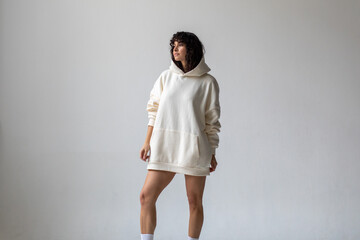 Brunette woman with curly hair in a white oversized hoodie and bare legs.
