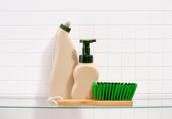 Cleanup and washing time. Beige detergent dispensers and a brush with thick green bristles on a...