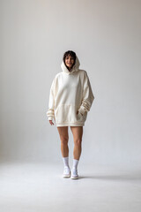 Fototapeta premium Brunette woman with curly hair in a white oversized hoodie and bare legs.
