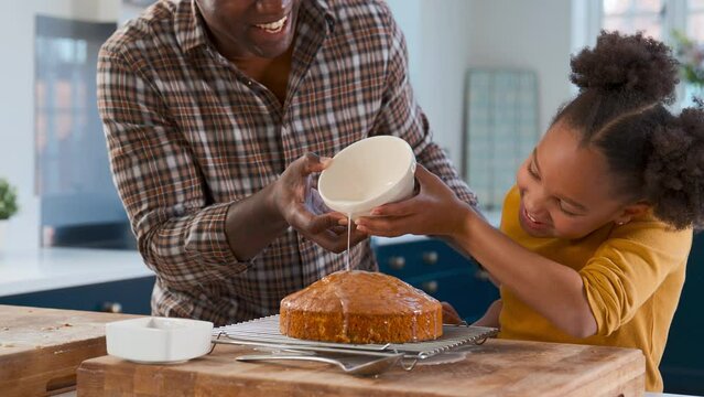Father and daughter baking at home in kitchen decorating homemade cake with icing - shot in slow motion