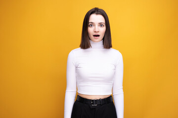 Surprised girl with her mouth open in the studio on a yellow background.