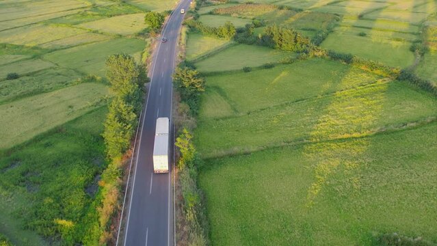 Aerial side shot of a truck with trailer on the road in beautiful countryside in the sunrise light