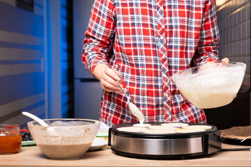 Woman cooking delicious crepe on electric pancake maker in kitchen, closeup
