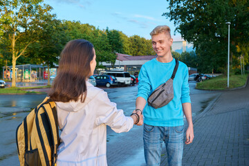 Teenage friends meeting outdoor, guy and girl shake hands