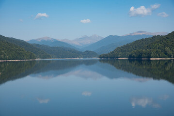 Smooth lake surface with beautiful reflection of cloudy sky and the hills are covered with dense forest