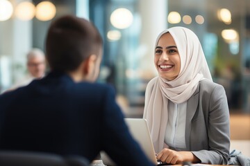 Smiling Middle eastern businesswoman wearing a hijab having a meeting conversation with a co-worker at the workplace