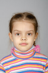 Close-up portrait of a disheveled five-year-old girl wearing a colored striped sweater on a gray background