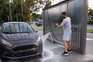 The front part of the car being washed by a man using a water cannon. A car at a self service car wash.