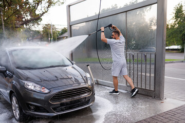 A man at the car wash whips the water cannon over his head and aims it at the windshield. A car at...