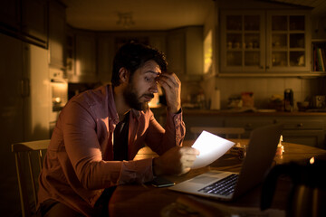 Worried Young Caucasian man going over bills and payments at night at home