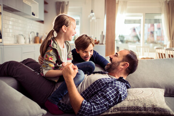 Young Caucasian father playing with his children and having fun on the couch in the living room at home