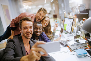 Diverse group of coworkers taking a selfie on a smartphone in the office of a startup company