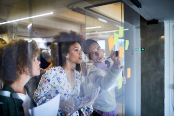 Young and diverse group of people going over ideas for a project and putting notes on a window in a startup company office