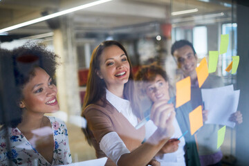 Young and diverse group of people going over ideas for a project and putting notes on a window in a...