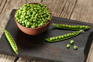 Green peas in closed and open pods, peeled peas in a bowl, scattered pea grains on a wooden background.