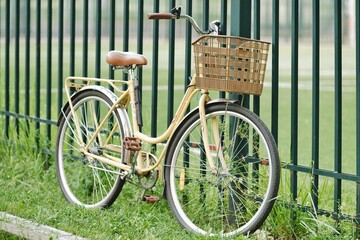 Vintage bicycle standing on the grass. Yellow retro bicycle with wicker basket.