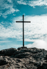 Naklejka premium Vertical shot of the cross on the top of the stony hill against a blue sky