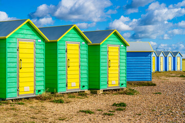Fototapeta na wymiar Colorfool beach huts on the shores of Littlehampton East Beach in Sussex, England, UK; wooden yellow, green and blue huts on pebbles beach