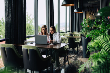Two female executives are sitting in a cafe and looking at their laptop