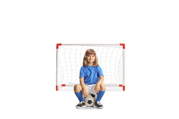 Little girl in a football kit sitting on a ball in front of a goal