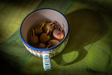 Medlar fruit in color cup on green tablecloth with shadow