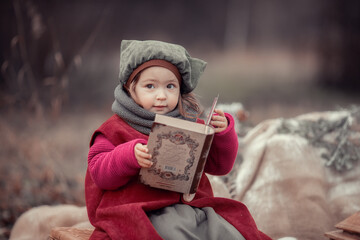 Little girl in red costume of elf sitting in woods with a book
