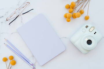 Flat lay of white marble table with stationery, glasses, yellow flowers and photo camera