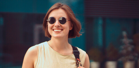 A girl in sunglasses with a smiley face walks around the city.
