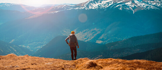 The traveler looks at the stunning view of the snow-capped mountains at sunset. Young man with a...