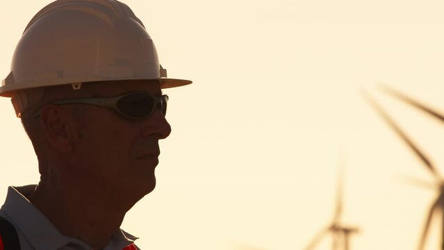 Silhouette of an engineer with white helmet in wind farm