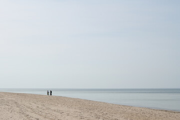 Pusta plaża morska. Dwie osoby spacerują w słoneczny dzień brzegiem morza. Złota polska...