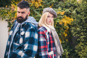 Stylish blonde beautiful woman and bearded man walking at autumnal golden garden. Hipster style. Sweater weather. Male and female standing back to back looking at camera.