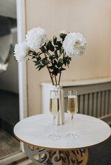Glasses of champagne, a vase of flowers stand on a wooden table indoors at a ceremony. Close-up wedding photography, design.