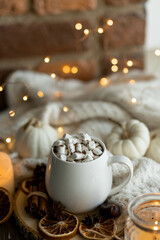 Autumn cozy home composition with hot chocolate with marshmallow and candles. Aromatherapy on a grey fall morning, atmosphere of cosiness and relax. Wooden background, window sill, close up.