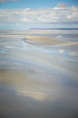 The view from Mont Saint Michel Abbey with a group of tourists crossing the bay waters during low tide. High view from the monastery walls. Vertical.
