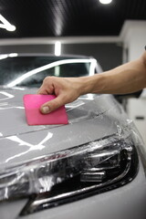 A car wrapping specialist applies a polyurethane film to the car. Selective focus. PPF protective film against chips and scratches. Car wrapping.  - obrazy, fototapety, plakaty