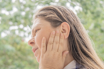 mature caucasian woman 50 years holding hand to sore ear, close up female face with facial...