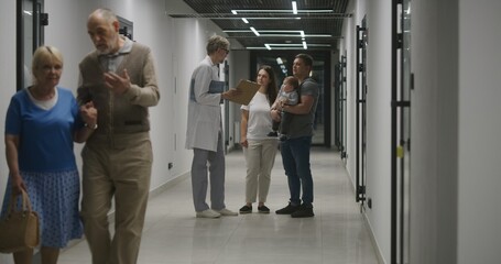 Doctor and family with little child stand in clinic corridor. Doctor talks to patients, discusses medical examination or test results. Medical staff and people in hospital, medical center. Healthcare.