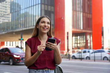 Fototapeta premium Brazilian business woman using her smartphone with ring holder walking on Paulista Avenue in Sao Paulo megalopolis, Brazil