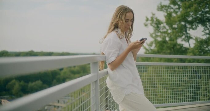 Smiling Woman Messaging Through Phone Leaning On Railing