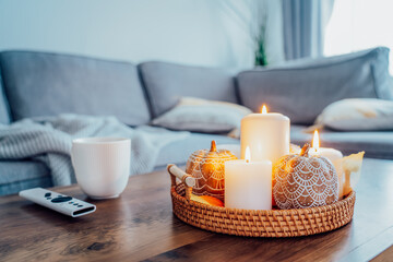 Autumn fall cozy mood composition for hygge home decor. Orange pumpkins, burning candles, cup with hot drink and remote controller on coffee table in living room. Movie night at home. Cozy relax time. - obrazy, fototapety, plakaty
